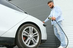 Mens Holding macht opladen kabel voor elektrisch auto in buitenshuis auto park. en hij s gaan naar aansluiten de auto naar de opladen station in de parkeren veel in de buurt de boodschappen doen centrum. foto