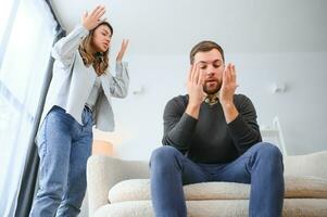 familie ruzie, Mens en vrouw zittend Aan sofa Bij huis. boos vrouw schreeuwt Bij haar man foto