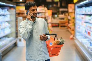 jong Mens gebruik makend van mobiel telefoon terwijl boodschappen doen Bij supermarkt foto