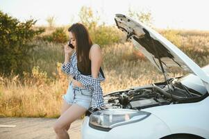 Dames pratend Aan de telefoon over probleem met haar auto ze kan niet. jong sexy meisje overlegt Aan de telefoon gedurende auto reparatie foto