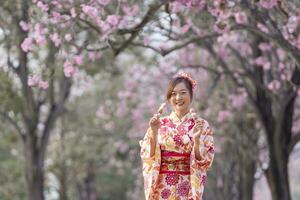 Japans vrouw in traditioneel kimono jurk Holding zoet Hanami dango toetje terwijl wandelen in de park Bij kers bloesem boom gedurende voorjaar sakura festival foto