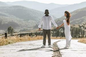 elegant model- paar in de bergen in zomer. een Mens in een darth vader pet en een meisje in een wit zijde jurk tegen de achtergrond van een Woud en berg pieken. foto