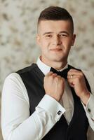 portret. een Mens in een wit shirt, zwart boog stropdas en zwart broek en hesje poses in een kamer. een elegant horloge. Mannen stijl. mode. bedrijf foto