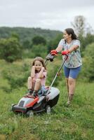 een vrouw in laarzen met haar kind in de het formulier van een spel maait de gras met een grasmaaier in de tuin tegen de achtergrond van bergen en mist, tuin gereedschap concept foto