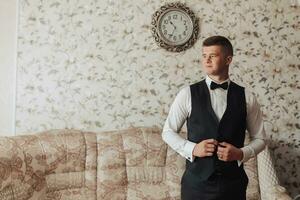 portret. een Mens in een wit shirt, zwart boog stropdas en zwart broek en hesje poses in een kamer. een elegant horloge. Mannen stijl. mode. bedrijf foto