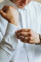 ochtend- van de bruidegom en details, wit shirt, mooi zo licht, jong Mens, elegant bruidegom krijgen gekleed, krijgen klaar voor de bruiloft ceremonie. detailopname van mannetje handen foto