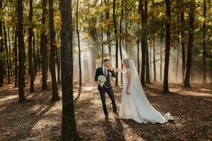 de bruid en bruidegom zijn dansen tegen de achtergrond van een sprookje mist in de Woud. de stralen van de zon breken door de rook, een sprookje bruiloft foto