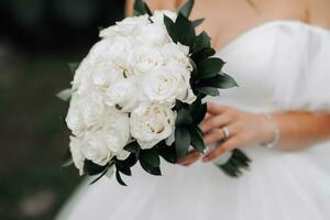 bijgesneden foto. de bruid is vervelend een wit jurk met een halslijn, Holding een boeket van wit rozen. mooi handen en zilver sieraden. Frans manicuren. portret van de bruid. foto