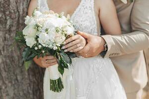 foto van een bruiloft boeket van wit bloemen en groen in de handen van de bruid en bruidegom. de bruidegom houdt de bruid hand. mooi handen. Frans manicuren. bruiloft ringen