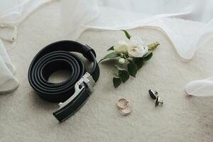 accessoires voor de bruidegom bruiloft. zwart riem, riem, enkelbandje, goud ringen, manchetknopen Aan grijs achtergrond. Mannen mode foto