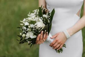 de bruid is Holding een mooi bruiloft boeket van wit bloemen. wit avond jurk, mooi sieraden Aan de hand- foto
