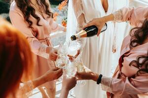 jong bruidsmeisjes zijn hebben pret en glimlachen in roze zijde Jurken drinken Champagne Bij de bruid Prieel. mooi Dames vieren een vrijgezellin partij, in een Prieel en met Champagne. foto