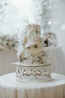 wit bruiloft taart met bloemen. mooi eigengemaakt drieledig bruiloft taart versierd met wit orchideeën in een rustiek stijl Aan een wit tafel foto