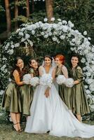 bruidsmeisjes glimlachen samen met de bruid. de bruid en haar pret vrienden vieren de bruiloft na de ceremonie in bij elkaar passen jurken. bruid en vrienden in natuur foto