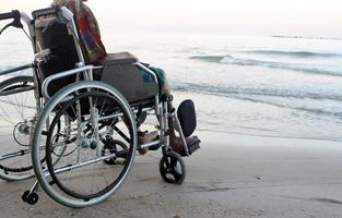 oude man in een rolstoel kijkt vanaf het strand naar de zee foto