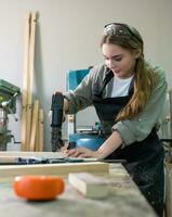 vrouw timmerman vervelend beschermend veiligheid bril en gebruik makend van elektrisch werk Aan een hout. artiest of meubilair ontwerper werken Aan een Product idee in een werkplaats. foto