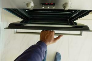 persoon hand- Open elektrisch oven deur Bij huis foto