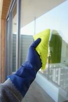 hand- in blauw handschoen schoonmaak venster met groen vod foto