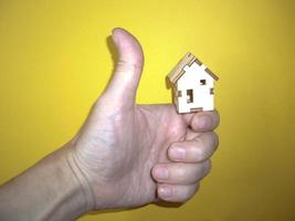 klein houten huis in de hand van een man op een gele achtergrond foto