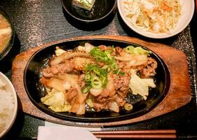 top visie van Japans voedsel heet pan gebakken varkensvlees met Japans saus met salade Aan zwart dienblad achtergrond. foto