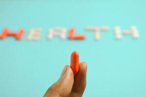 mannetje hand- houden rood pil, achtergrond Gezondheid woord van kleurrijk geneeskunde pillen, supplement, vitamine, kleurrijk foto