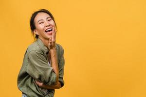 jonge azië dame met positieve uitdrukking, breed glimlachen, gekleed in casual kleding en camera kijken over gele achtergrond. gelukkige schattige blije vrouw verheugt zich over succes. gezichtsuitdrukking concept. foto