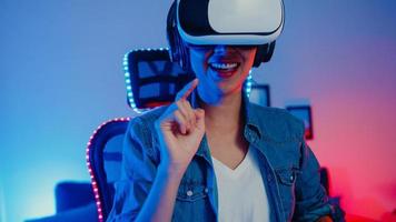 gelukkig aziatisch meisje draagt virtual reality-bril bril headset voelt verrassing echt spelprogramma 's nachts in haar neon-thuisstudio, jonge vrouw raakt de lucht aan, de vr-ervaring, thuisquarantaine-activiteit. foto