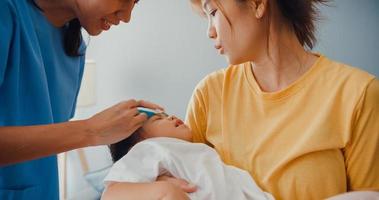 jonge azië vrouwelijke kinderarts bevestigt de koortswerende gel op het voorhoofd van de baby patiënt bezoek arts met moeder in de woonkamer thuis. medische zorgverzekering, behandeling en gezondheidszorgconcept. foto