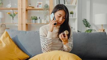 zieke jonge aziatische vrouw houdt medicijnen vast op de bank gebruik smartphone-oproep om thuis met de arts te overleggen. meisje neemt medicijnen in na doktersbevel, quarantaine thuis, social distancing coronavirus concept. foto