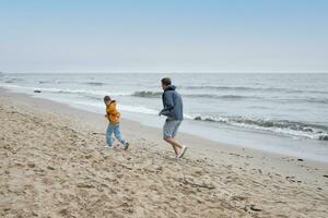 vader en zijn zoon pret Speel Aan de herfst strand. koel herfst het weer. foto