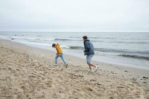 vader en zoon Speel en rennen Aan de herfst strand. koel herfst het weer. foto