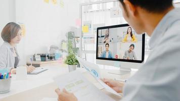 Aziatische zakenmensen die desktop gebruiken, praten met collega's die zakelijke brainstorm over plan bespreken in een videogesprekvergadering in een nieuw normaal kantoor. levensstijl sociale afstand en werk na het coronavirus. foto