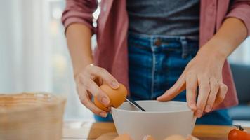 handen van jonge Aziatische vrouw chef-kok kraken eieren in keramische kom koken omelet met groenten op houten bord op keukentafel in huis. levensstijl gezond eten en traditioneel bakkerijconcept. foto