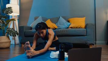 jonge aziatische dame in sportkledingoefeningen die aan het trainen zijn en laptop gebruiken om thuis een yogavideo-tutorial te bekijken. afstandstraining met personal trainer, sociale afstand, online onderwijsconcept. foto