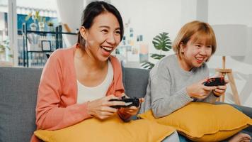 lesbische lgbtq-vrouwen spelen thuis een videogame. jonge Aziatische dame met behulp van draadloze controller met grappig gelukkig moment samen op de bank in de woonkamer. ze hebben een geweldige en leuke tijd om vakantie te vieren.