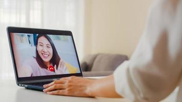 jonge Aziatische zakenvrouw met behulp van laptop videogesprek praten met vrienden tijdens het werken vanuit huis in de woonkamer. zelfisolatie, sociale afstand, quarantaine voor coronavirus in het volgende normale concept. foto
