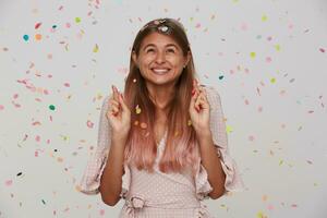 gelukkig jong mooi vrouw met licht bruin lang haar- vieren haar verjaardag en maken wens met gekruiste vingers, hebben mooi hoor partij met haar vrienden en staand in papier confetti foto