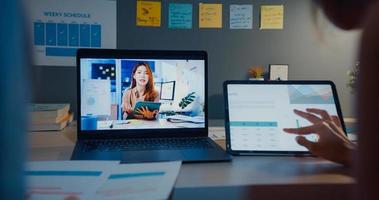 jonge Aziatische financiële student dames kijken les online en studeren 's nachts met laptop en tablet in de woonkamer vanuit huis. aantekeningen maken terwijl je naar het computerscherm kijkt, leer online concept. foto