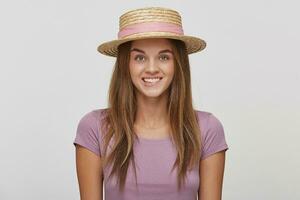 grappig vrolijk blij jong meisje in een rietje hoed met een roze lint, looks speels, beetje een lager lip, gekleed lavendel t-shirt, over- wit achtergrond foto