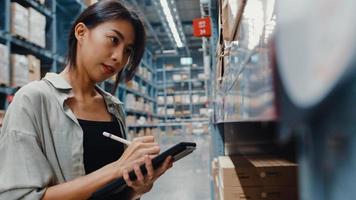 aantrekkelijke jonge azië zakenvrouw manager op zoek naar goederen met behulp van digitale tablet controleren voorraadniveaus staan in retail shopping center. distributie, logistiek, pakketten klaar voor verzending. foto