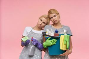 portret van uitgeput jong withoofdig Dames maken voorjaar schoonmaak en wezen moe na Dat, Holding flessen met huishouden Chemicaliën, geïsoleerd over- roze achtergrond foto