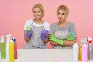 binnen- schot van jong bruine ogen blond huisvrouwen vervelend eenvoudig t-shirts en schorten met dots terwijl poseren over- roze achtergrond, maken voorjaar schoonmaak met huishouden Chemicaliën foto