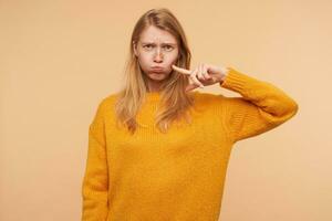 portret van jong aantrekkelijk vrouw met los foxy haar- puffend uit haar wangen en fronsen wenkbrauwen terwijl op zoek Bij camera, geïsoleerd over- beige achtergrond foto