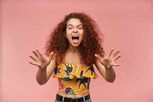 portret van boos, roodharige meisje met gekruld haar. vervelend kleurrijk off-shoulder blouse. mensen en emotie concept. boos uit, had genoeg. aan het kijken Bij de camera geïsoleerd over- pastel roze achtergrond foto