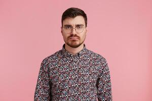 studio schot van verdrietig jong gebaard Mens in bril, vervelend in een kleurrijk shirt, geïsoleerd over- roze achtergrond. mensen en emoties concept. foto