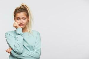 detailopname van verdrietig verveeld jong vrouw met blond haar- en paardenstaart draagt blauw sweater looks moe en depressief geïsoleerd over- wit achtergrond foto