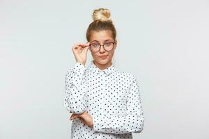 portret van ongelukkig verdrietig jong vrouw met bun draagt polka punt overhemd en bril voelt teleurgesteld en houdt handen gevouwen geïsoleerd over- wit achtergrond foto