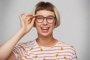 detailopname van gelukkig mooi jong vrouw draagt gestreept t overhemd en bril voelt ontspannen, lachend en looks direct in camera geïsoleerd over- wit achtergrond foto