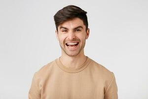 studio foto van een aantrekkelijk charmant vrolijk glimlachen brunette gekleed in naakt trui geïsoleerd Aan een wit achtergrond. de vent is verheugd met zijn succes verheugt zich in zijn zege.