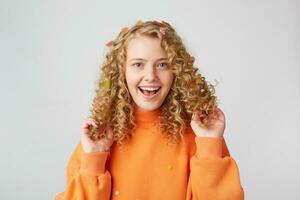 een tijd naar hebben plezier. portret van een heel gelukkig meisje in oranje trui accenten Toneelstukken met haar gekruld haar, glimlachen geïsoleerd Aan een wit achtergrond foto